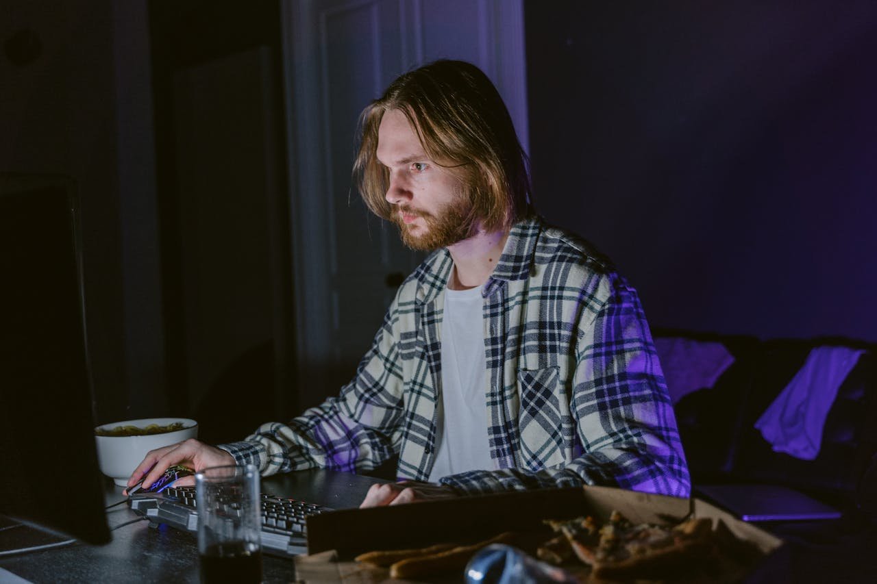 Young man intensely gaming on a computer in a dimly lit room at night.