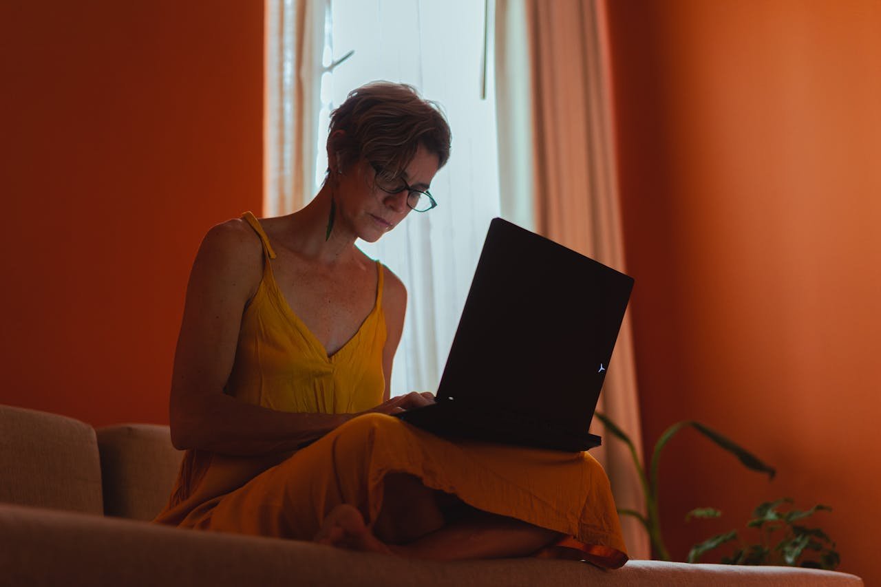 A senior woman works on her laptop indoors, reflecting positive aging and modern freelance work.