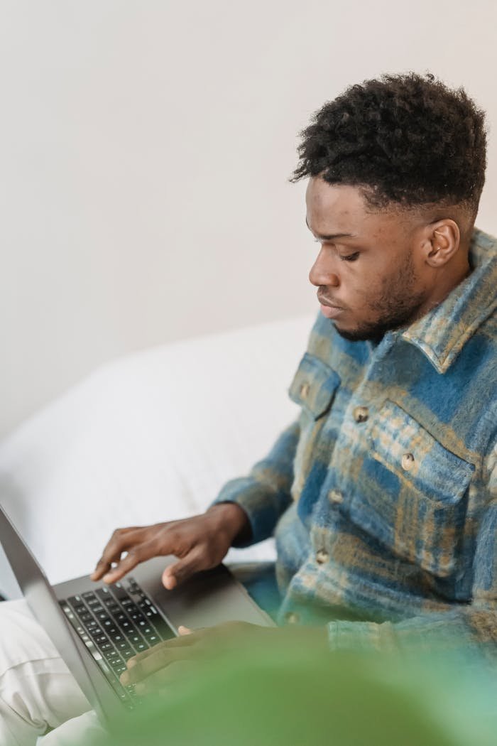 A young man deeply focused while working on a laptop from his comfortable living room.